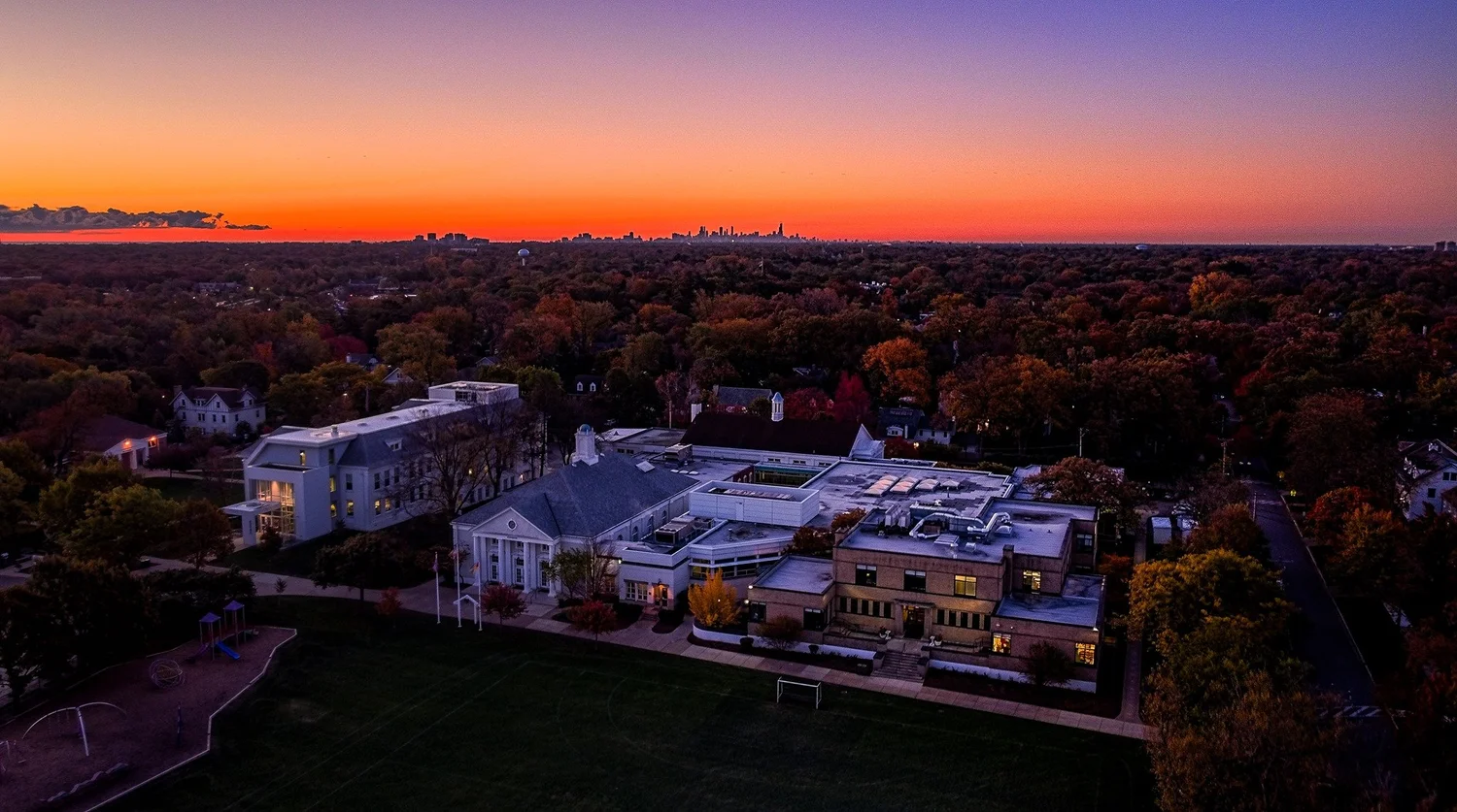 Aerial view of the North Shore Country Day School campus at dusk, with the Chicago skyline on the horizon